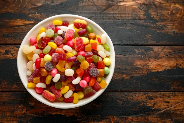 A mix of colorful candy in white bowl on wooden table — Stock Photo, Image