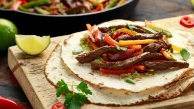 Biber, soğan ve ahşap tahtada avokado karışımlı biftek Fajitas.