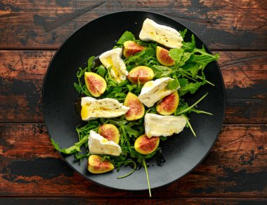 Vejetaryen peyniri, incir ve Arugula. Siyah tabakta servis edilen sıcak roket salatası.