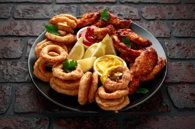 Yapış yapış tavuk kanatları ve limon, ketçap ve hardalla servis edilen yağda kızartılmış soğan halkaları. Yağlı, fast food konsepti