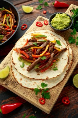 Biber, soğan ve ahşap tahtada avokado karışımlı biftek Fajitas.