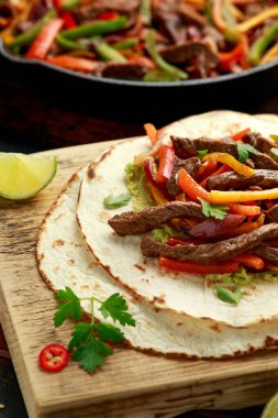 Biber, soğan ve ahşap tahtada avokado karışımlı biftek Fajitas.