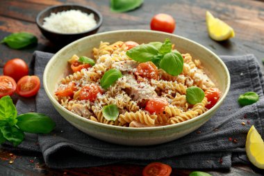 Sağlıklı tavuk, domatesli fusilli makarna, fesleğen ve parmesan peyniri. Tahta masada..