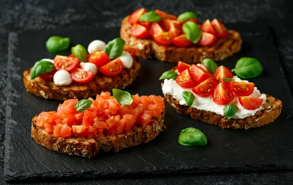 Bruschetta met ricotta, mozzarella kaas, basilicum, kers en gesneden tomaat op rustieke stenen plank — Stockfoto