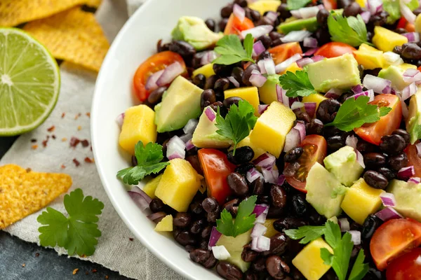 Avocado, salată de mango cu fasole neagră, roșii, ceapă roșie și chipsuri de tortilla. alimente sănătoase — Fotografie, imagine de stoc