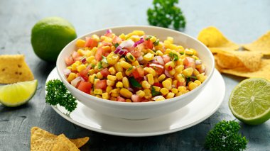 Meksika Corn Salsa 'sı beyaz kâse içinde limon ve tortilla cipsi. Sağlıklı yemek.