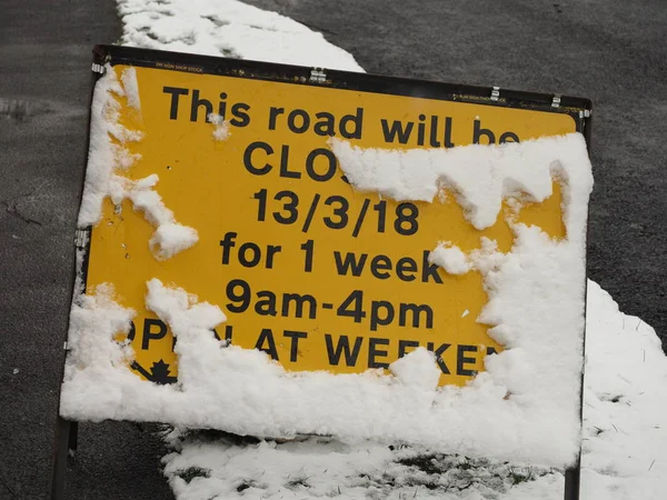 a temporary road closure sign half covered in snow