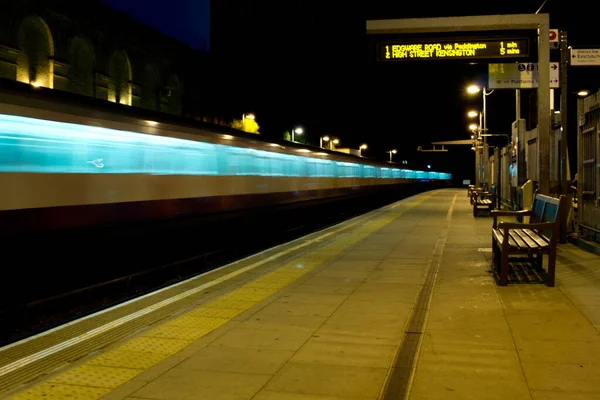 Nachtaufnahme eines U-Bahn-Zuges, der an einem Bahnsteig in London vorbeirast — Stockfoto