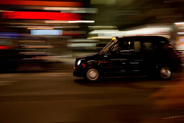 A black London taxi at night seen with motion blur against blurred neon lights — Stock Photo, Image