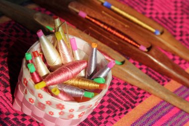 colorful bobbins in basket and wooden bobbin on silk fabric clipart
