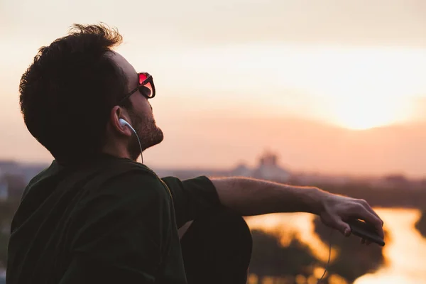 Νεαρός απολαμβάνοντας ηλιοβασίλεμα ακούγοντας τη μουσική από το smartphone — Φωτογραφία Αρχείου