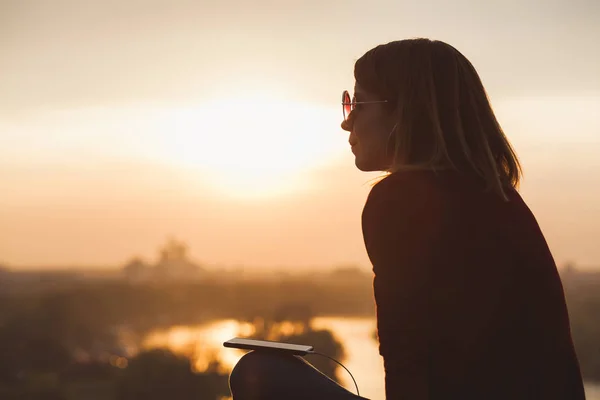 Mujer joven disfrutando de la puesta de sol escuchando la música en el teléfono inteligente — Foto de Stock