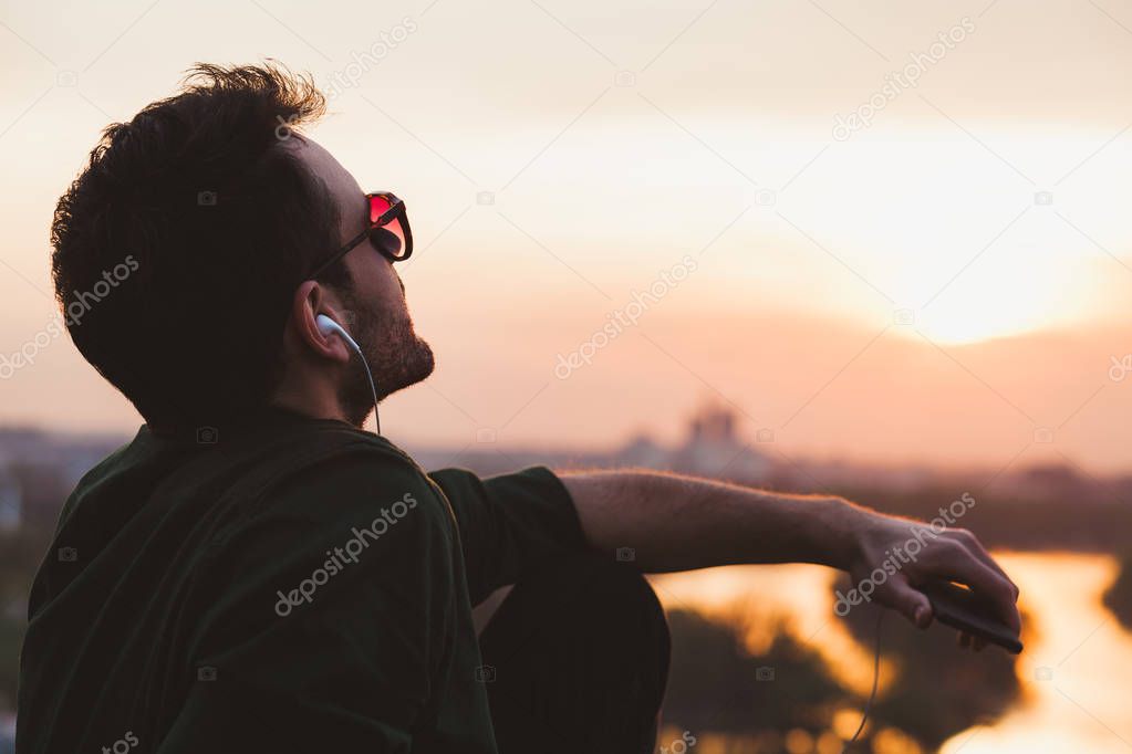 Young man enjoying sunset listening to the music on the smartphone