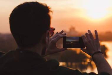 Genç adam onun Smartphone'da Günbatımı Fotoğraf çekimi