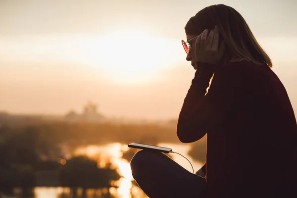 Jovem mulher desfrutando do pôr do sol ouvindo a música no smartphone — Fotografia de Stock