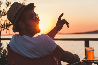 Genç adam bir sahil bar gün batımında zevk