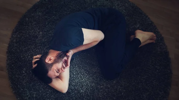Молодой человек с болью лежит на полу — стоковое фото