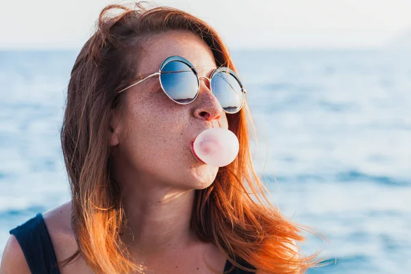 Young woman blowing bubble gum by the sea — Stock Photo, Image