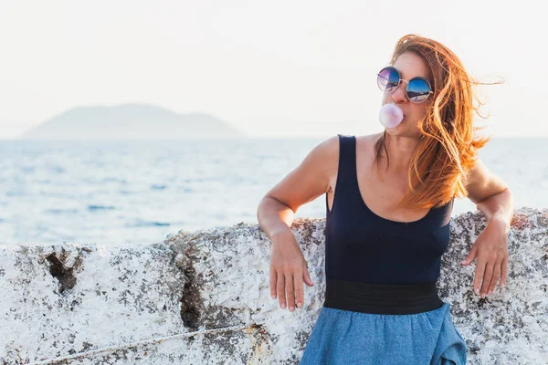 Mujer joven soplando goma de mascar junto al mar — Foto de Stock