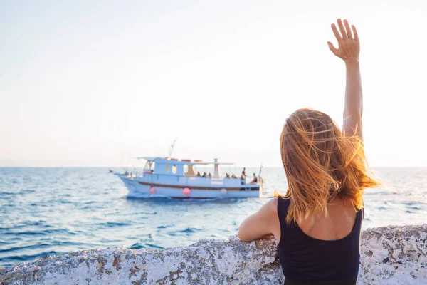 Young woman waving to a boat from the pier — Stock Photo, Image