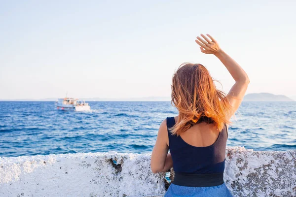 Young woman waving to a boat from the pier — Stock Photo, Image