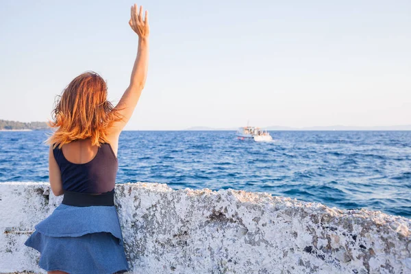 Young woman waving to a boat from the pier — Stock Photo, Image