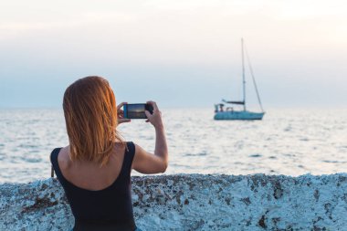 Genç kadın turist alarak fotoğraf ile deniz kenarında smartphone