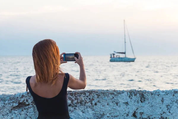 Young woman tourist taking photo with smartphone by the sea — Stock Photo, Image