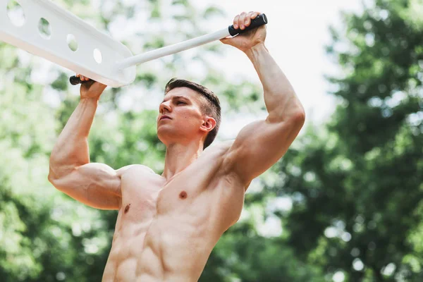 Pull ups egzersizleri yapıyor kas genç adam üzerinde bar