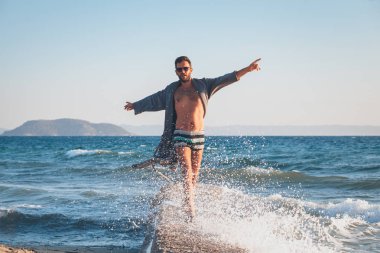 Mutlu genç adam üstünde belgili tanımlık rıhtım sahilde dans