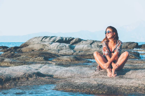 坐在岩石上享受日光浴的年轻女子在海边 — 图库照片