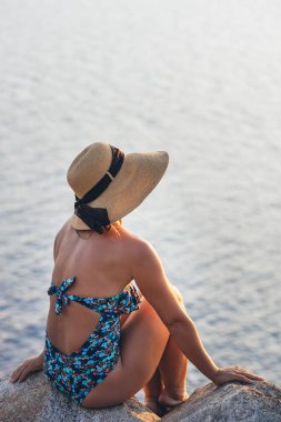 Genç bir kadın deniz kıyısındaki uçurumda gün batımının tadını çıkarıyor.