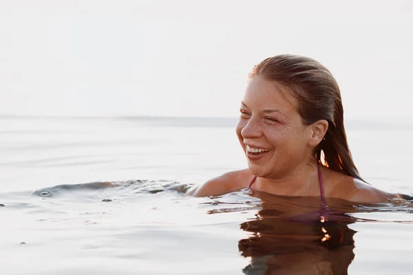 Young happy woman floating in the sea in sunset