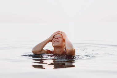 Genç mutlu kadın gün batımında denizde yüzüyor.