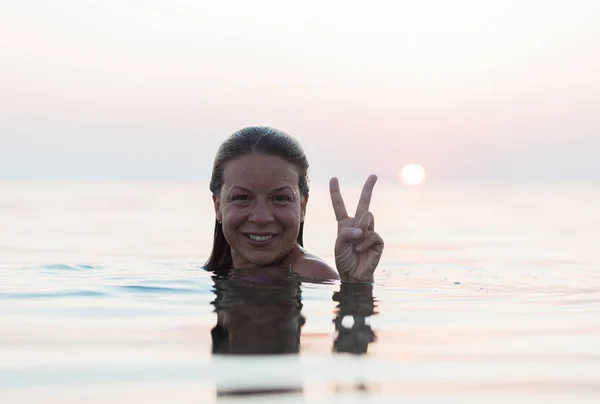 Ung Kvinne Som Svømmer Havet Solnedgang Lager Fredskilt Med Hånden – stockfoto