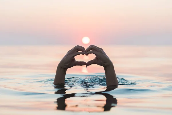 Hands making a heart shape on the water surface in sunset