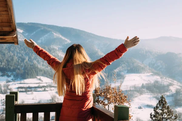 Elleri havada, kışın dağlara bakan bir kadın.