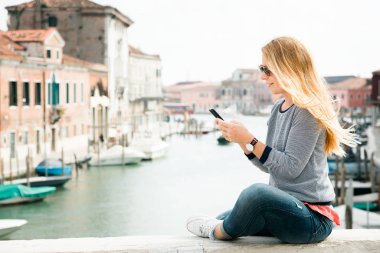 Venedik, İtalya 'daki Murano adasındaki köprüde akıllı telefon kullanan genç bir bayan gezgin.