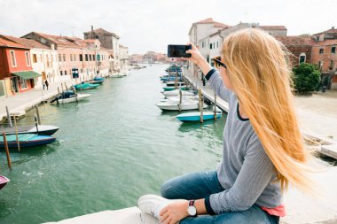 İtalya, Venedik 'te Murano köprüsünde telefonu alan genç bir kadın.