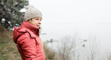 Genç bir kadın kış sabahı nehrin kenarında duruyor.