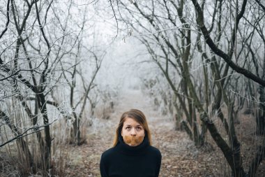 Soğuk kış ormanlarında ağzında bant olan bir kadın.