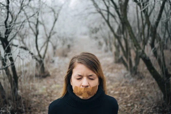 Woman with tape on her mouth in cold winter forest
