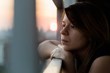Young sad woman looking outside through balcony of an apartment building clipart