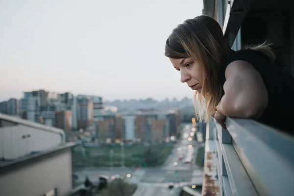 年轻悲伤的女人从一幢公寓楼的阳台往外看 — 图库照片