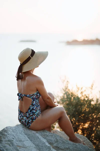 夕日を楽しむ海のそばの岩の上に座っている若い女性 — ストック写真