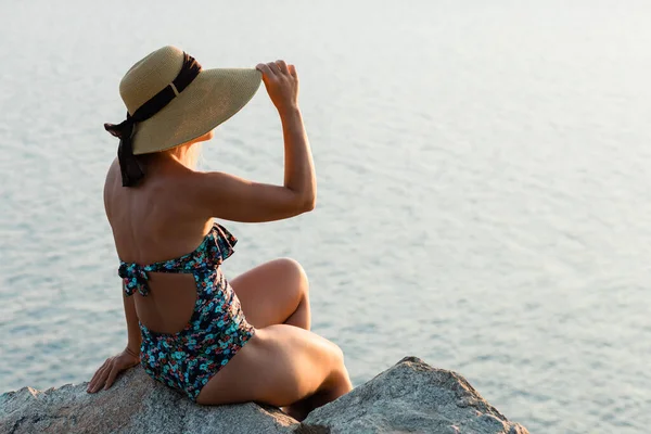 夕日を楽しむ海のそばの岩の上に座っている若い女性 — ストック写真