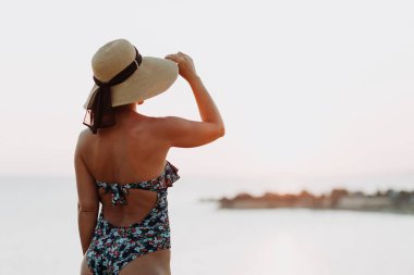 Deniz kenarında gün batımının tadını çıkaran genç kadın.