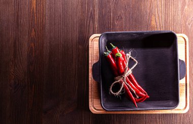 Kırmızı biberler dökme demir tavaya yerleştirilmiş. Kesme tahtası ve yazı için yeri olan ahşap zemin..