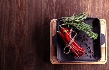 Biberiye, karabiber, kırmızı biber dökme demir tavaya yerleştirilmiş kesme tahtası ve yazı için yeri olan ahşap zemin..