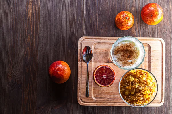 Tahtada sunulan sağlıklı kahvaltı kompozisyonu. Yanında yoğurt, meyve, mısır gevreği.